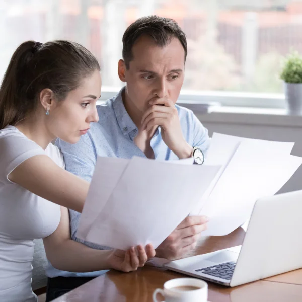 Un homme et une femme examinent des documents sur un ordinateur portable, discutant d'un prêt personnel avec un mauvais crédit.