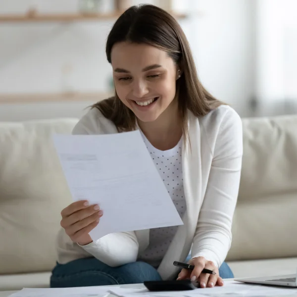 Femme lisant des documents sur un canapé, illustrant un prêt sans enquête de crédit.
