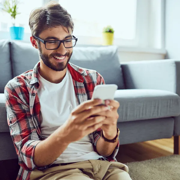 Un homme en lunettes est assis par terre et utilise son téléphone