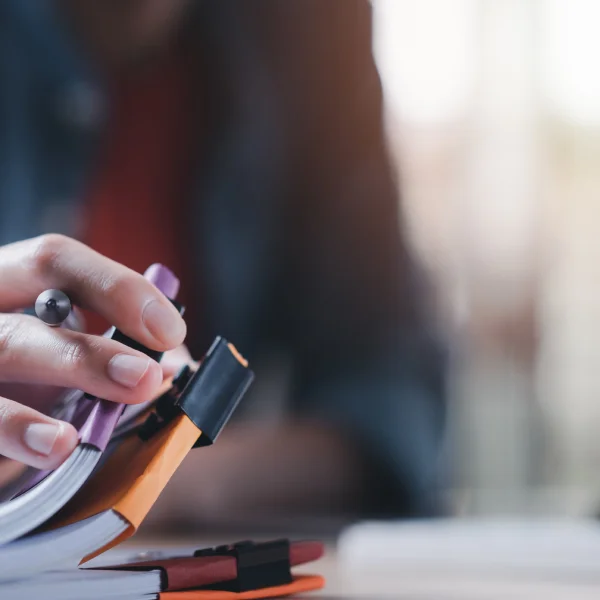 Une personne rédige une demande de prêt en ligne dans un carnet avec un stylo.